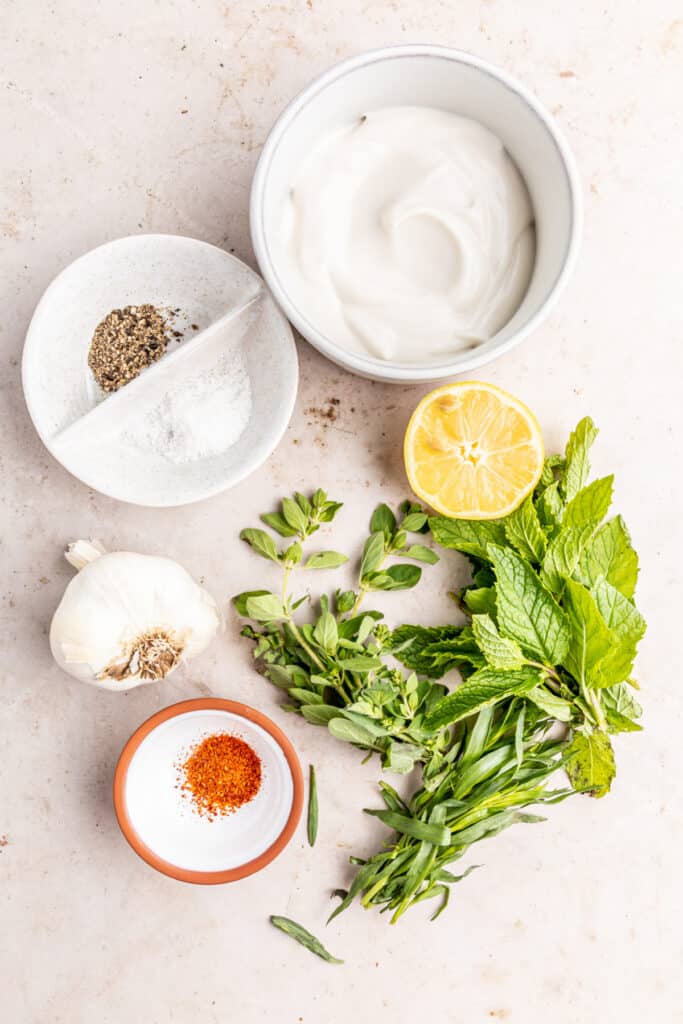 Ingredients for creamy herb sauce in a food processor, including yogurt, fresh herbs, garlic, and seasonings.