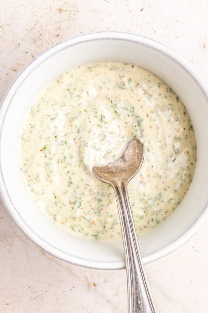 Finished creamy herb yogurt sauce in a bowl with a spoon, ready for drizzling.