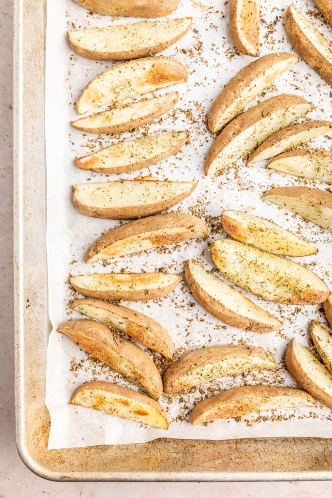Seasoned potato wedges arranged on a baking sheet lined with parchment paper, ready to roast.