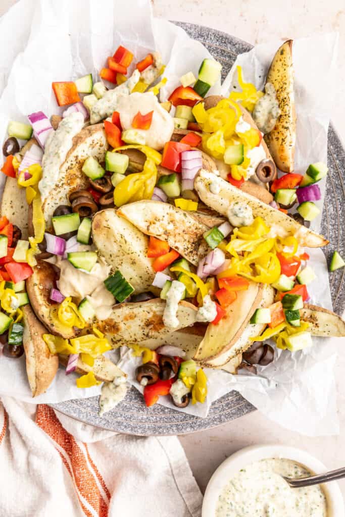Close-up of loaded fries with banana peppers, cucumbers, red onion, olives, and herb sauce.