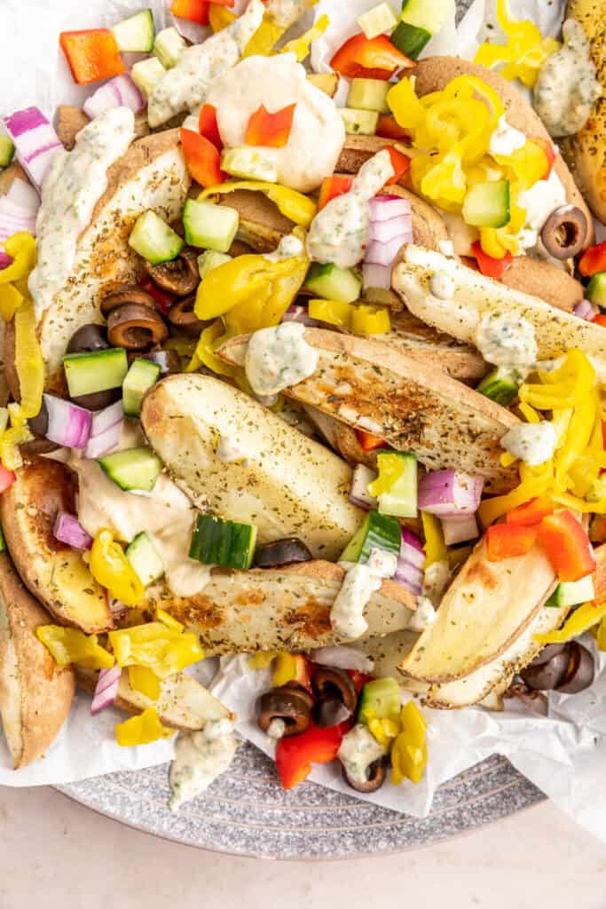 Extreme close-up of potato wedges with baba ganoush, creamy herb sauce, and fresh Mediterranean toppings.