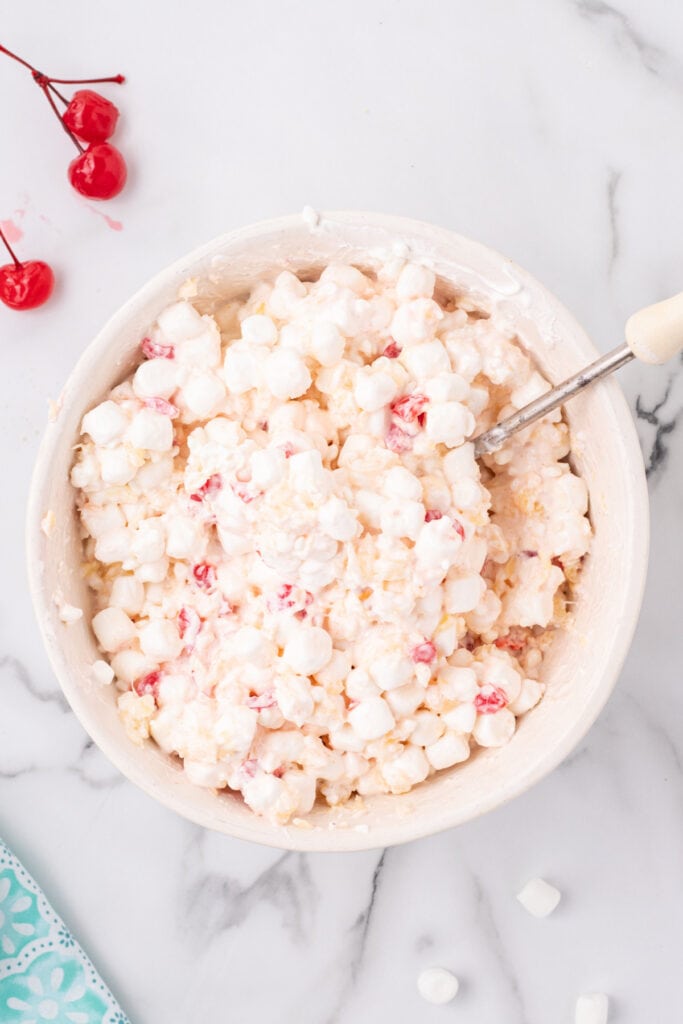 Mixed fruit salad in a bowl showing a creamy, fluffy texture with marshmallows, cherries, and pineapple visible throughout.