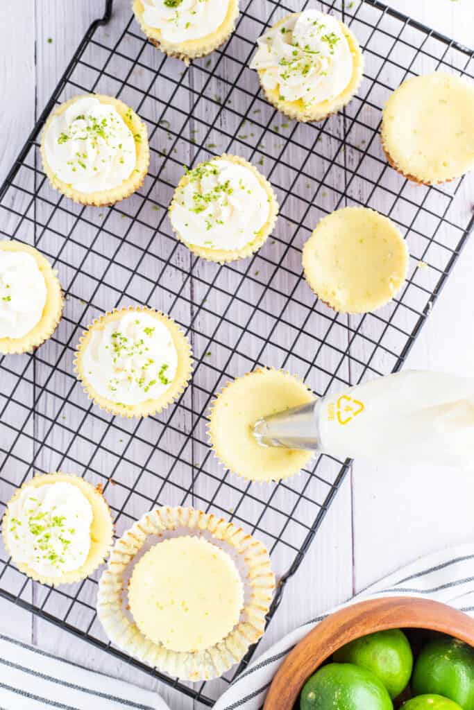 Mini key lime cheesecakes on a cooling rack with whipped cream being piped on top