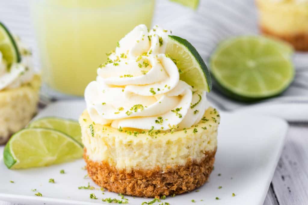 Mini key lime cheesecake on a plate, topped with whipped cream and a lime slice