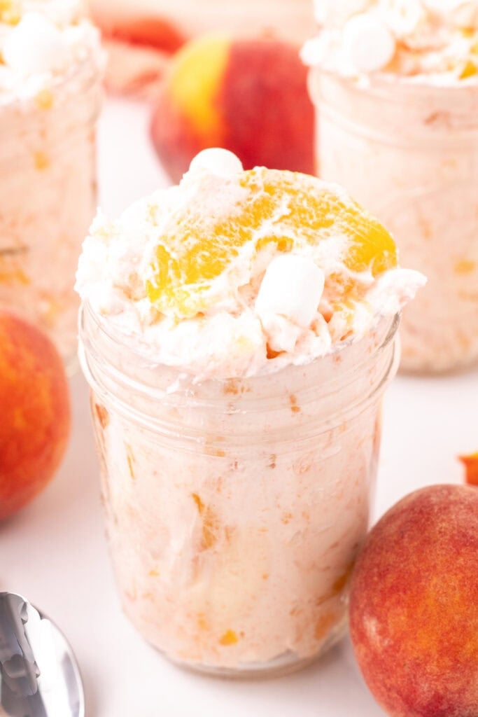 Mason jar filled with peach fluff salad next to fresh peaches