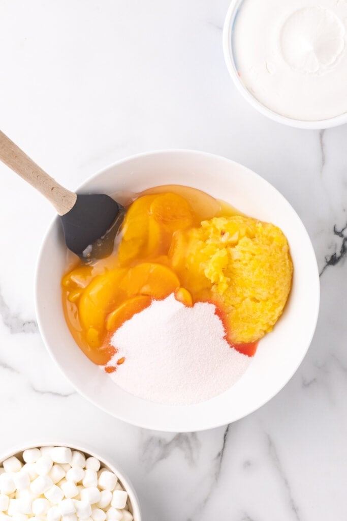 Bowl with peach pie filling, crushed pineapple, and peach gelatin being mixed.