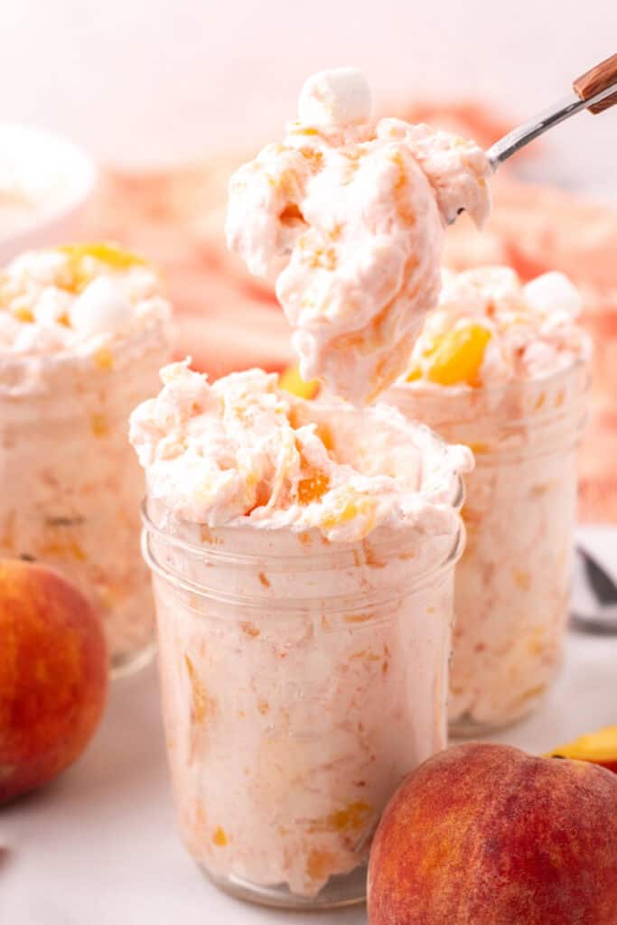 Spoonful of peach fluff salad being lifted from a jar with more jars in view.