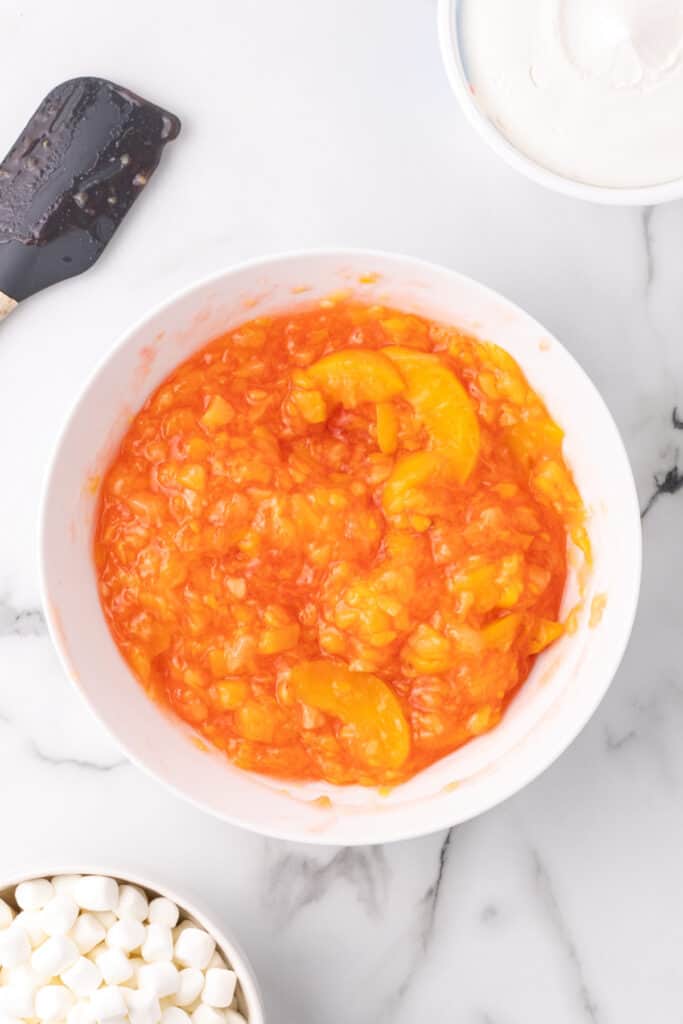 Peach fluff mixture of gelatin, pie filling, and pineapple partially stirred.