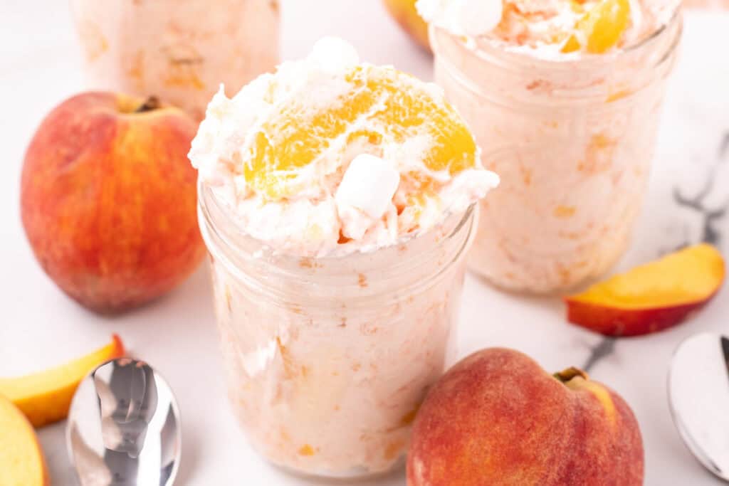 Close-up of peach fluff salad in a mason jar with peaches and marshmallows.