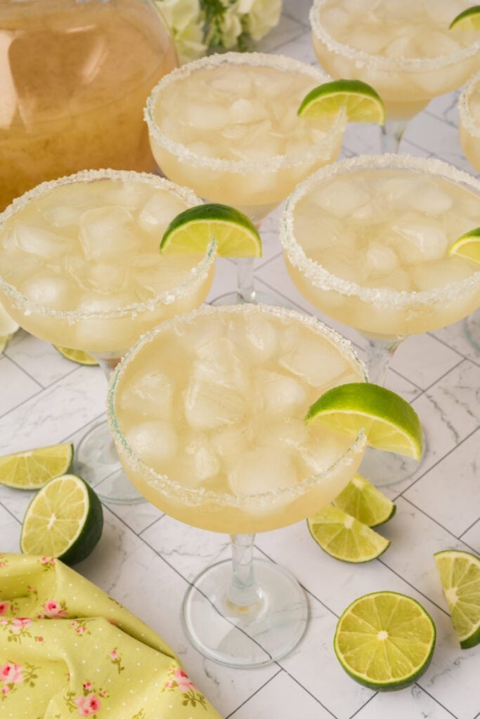 Group of margarita glasses filled with ice and garnished with lime wedges, ready to serve