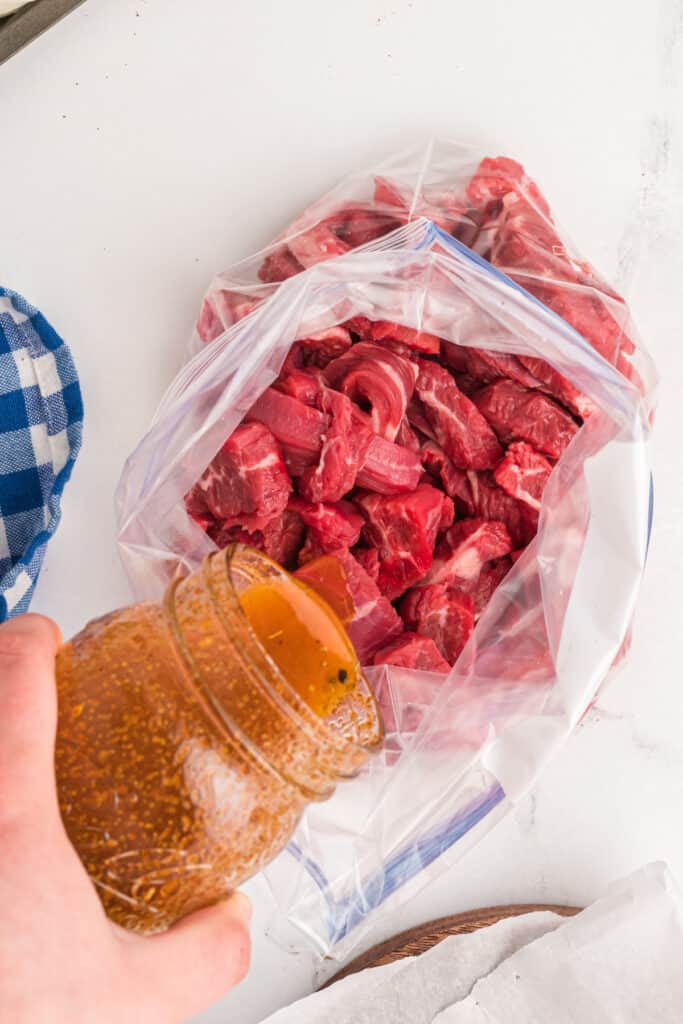 Marinated steak being poured into a plastic bag filled with sliced flank steak for fajitas