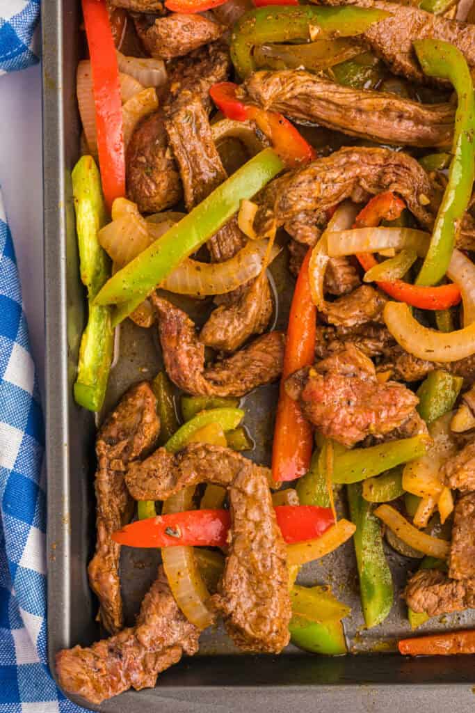 Cooked steak fajitas fresh out of the oven with browned steak, peppers, and onions on a sheet pan.