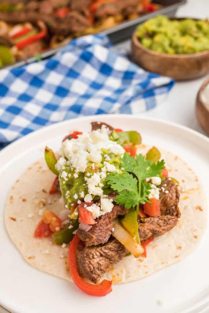 Close-up of a steak fajita taco topped with guacamole, pico de gallo, cilantro, and crumbled cheese.