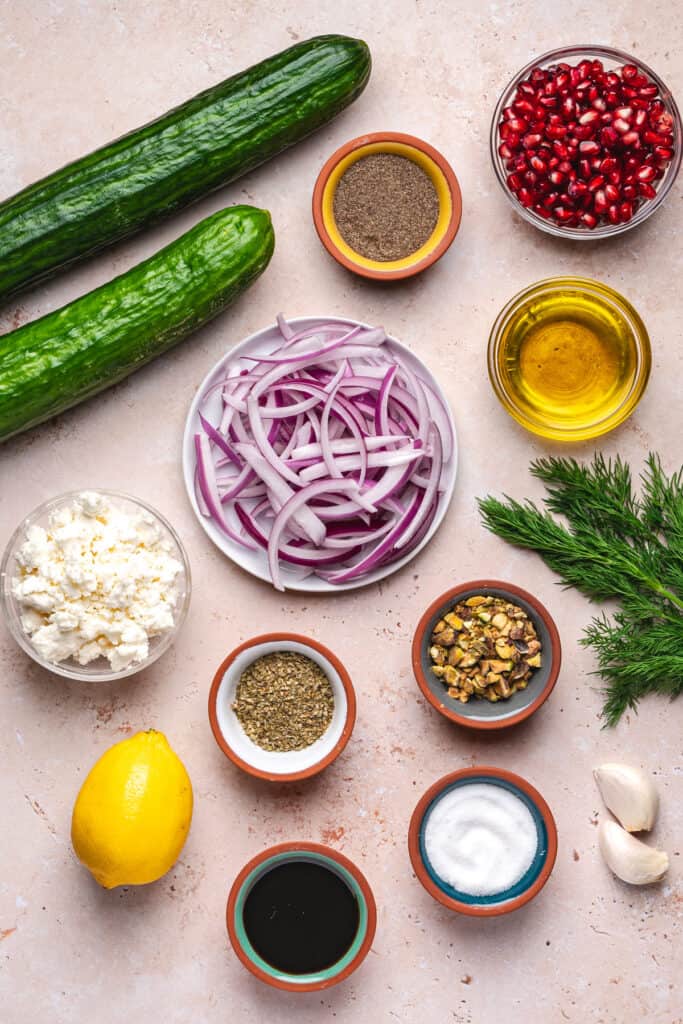 Overhead shot of all salad ingredients laid out, including cucumbers, onion, feta, dill, lemon, and spices