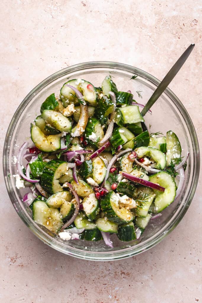 Mixed cucumber salad in a glass bowl with dressing visibly coating the ingredients