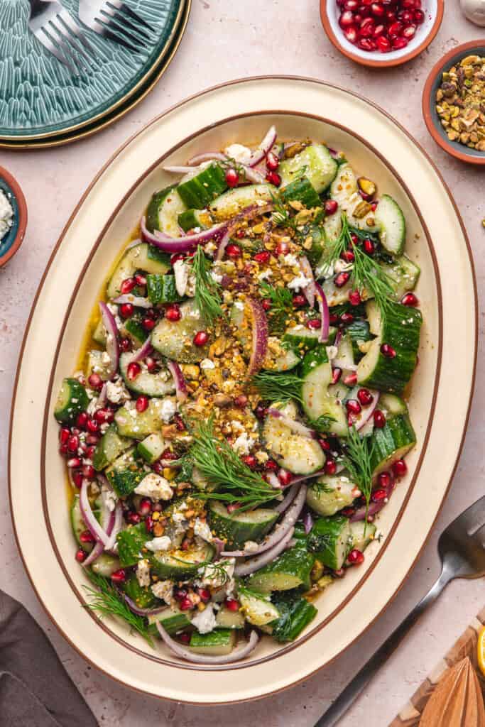 Final plated salad on a large oval dish, garnished with pistachios, dill, and pomegranate seeds