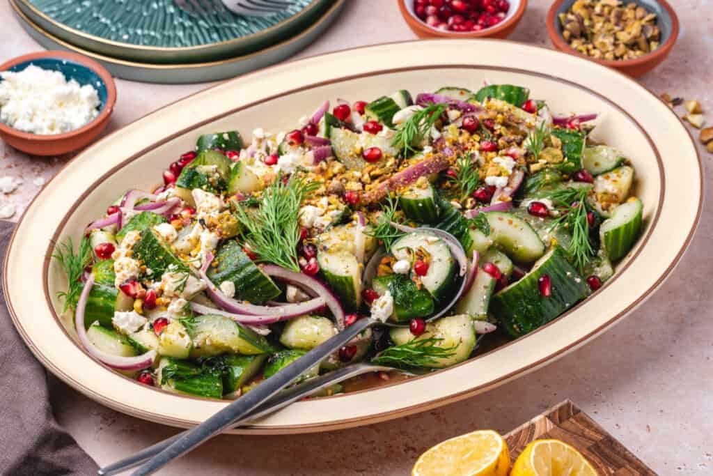 Side angle view of plated cucumber salad topped with dill, feta, pomegranate, and pistachios