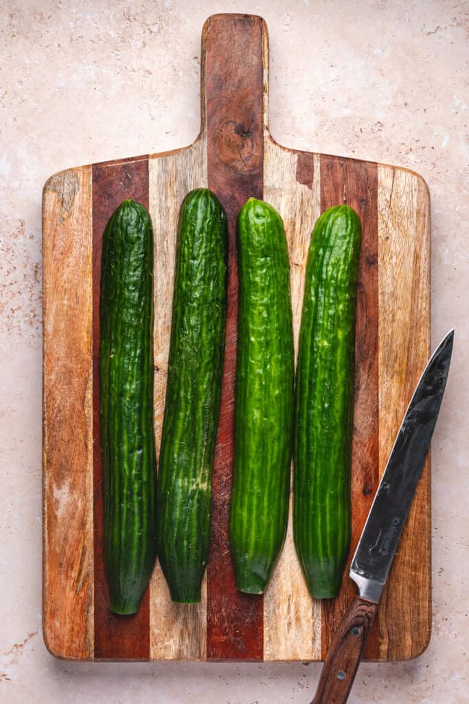 Four cucumber halves placed on a wooden cutting board with a knife beside them