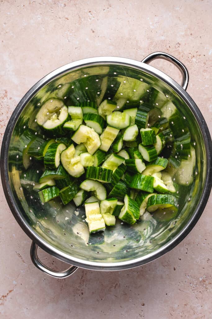 Smashed cucumber chunks draining in a metal colander