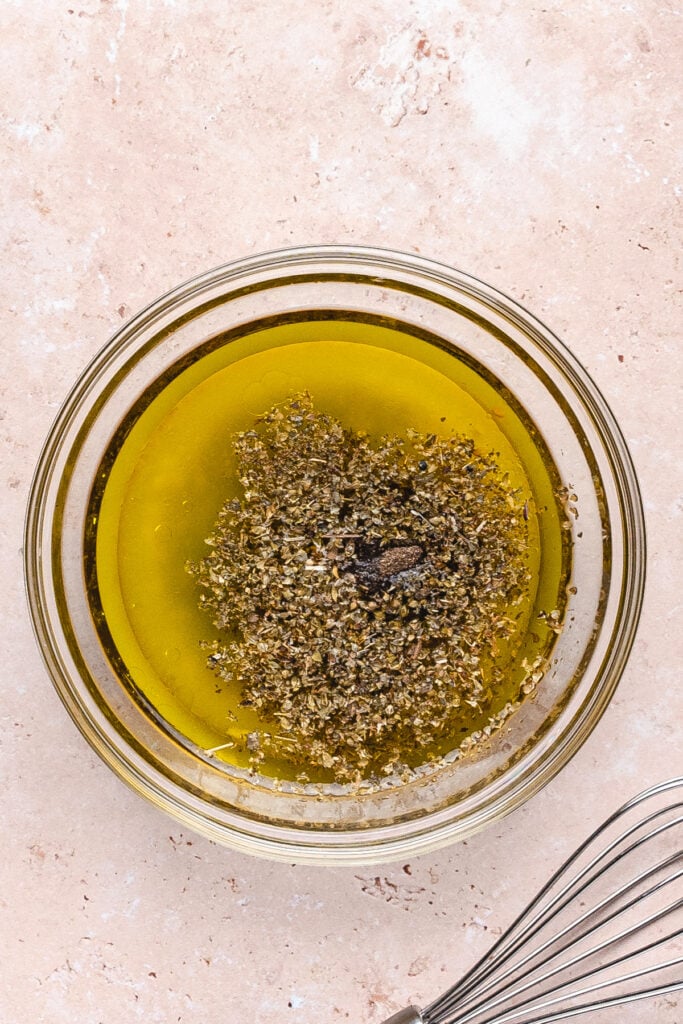 Bowl of olive oil with dried herbs and pepper, ingredients for the dressing