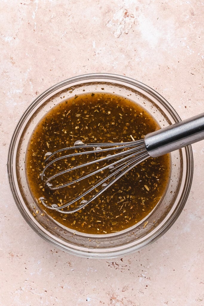 Whisked pomegranate dressing in a glass bowl with herbs blended in