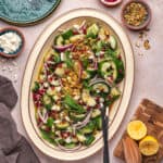 Overhead square image of smashed cucumber salad in a large platter, surrounded by ingredients and serving tools