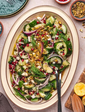 Overhead square image of smashed cucumber salad in a large platter, surrounded by ingredients and serving tools