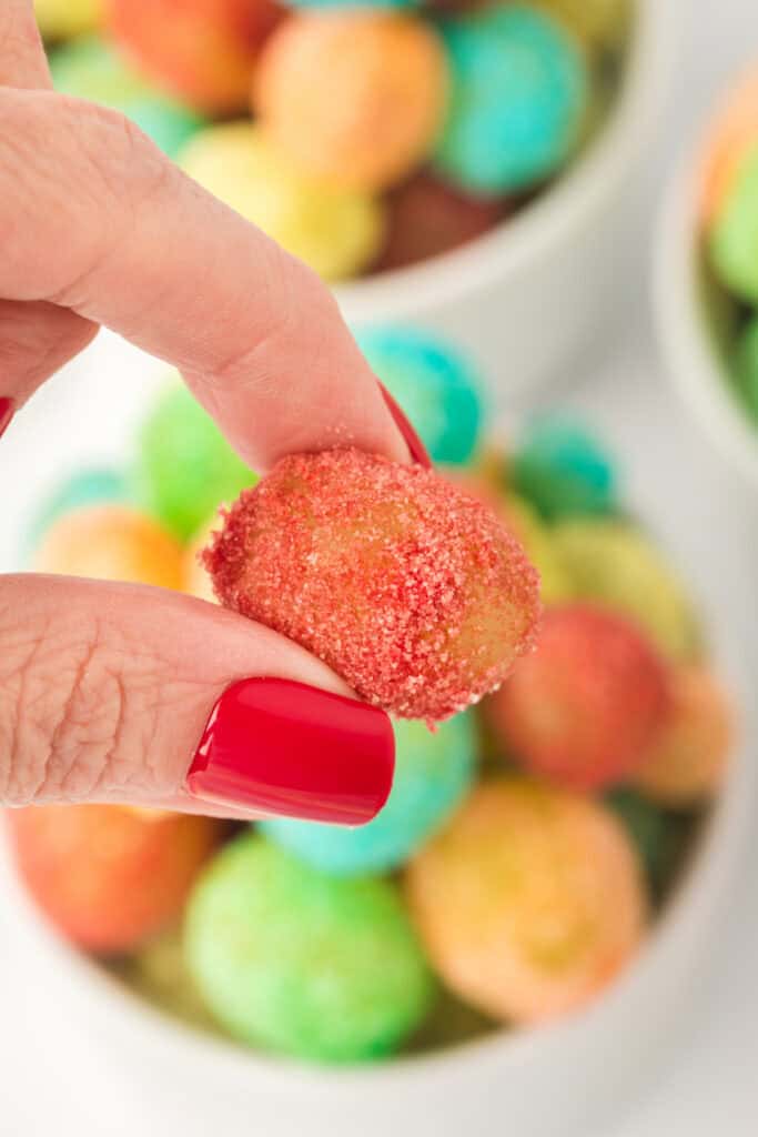 Close-up of a hand holding a red-coated Sour Patch Grape with bright red nails and colorful grapes in the background