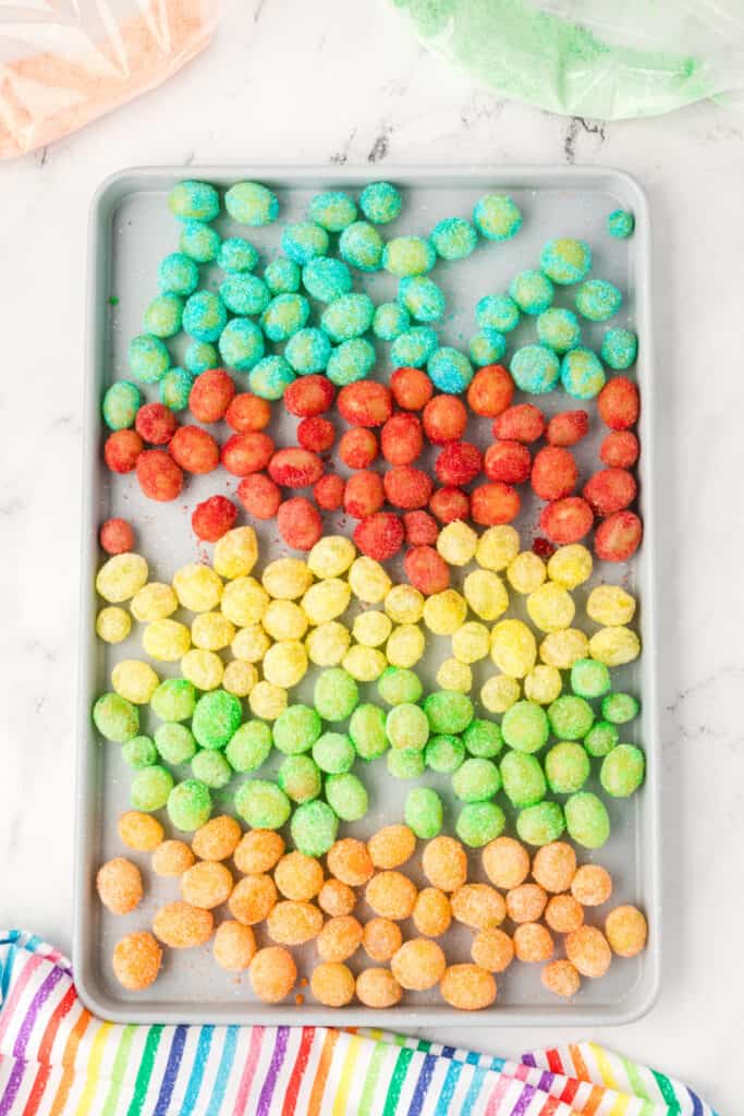 Baking sheet filled with rainbow-colored Sour Patch Grapes arranged by color on a white background