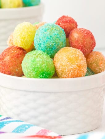 Square crop of a white ramekin filled with vibrant Sour Patch Grapes on a striped rainbow napkin