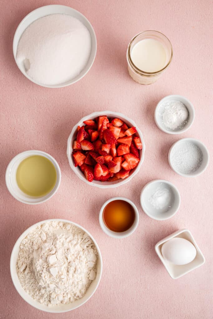 Overhead view of strawberry bread ingredients arranged on a pink background