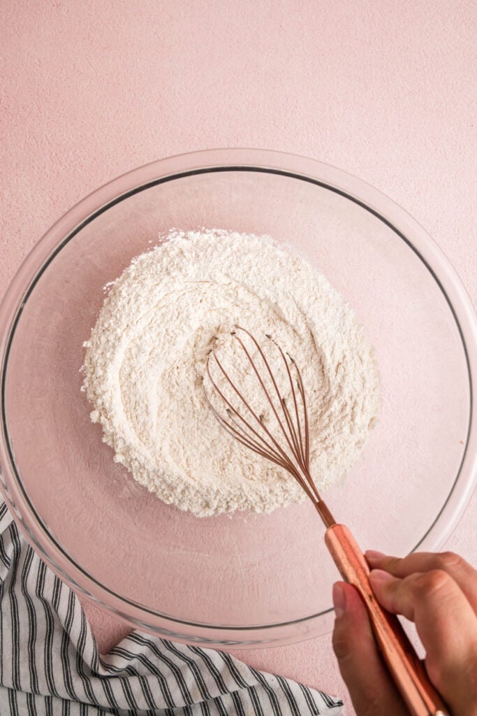 Hand using a whisk to combine dry ingredients in a glass mixing bowl