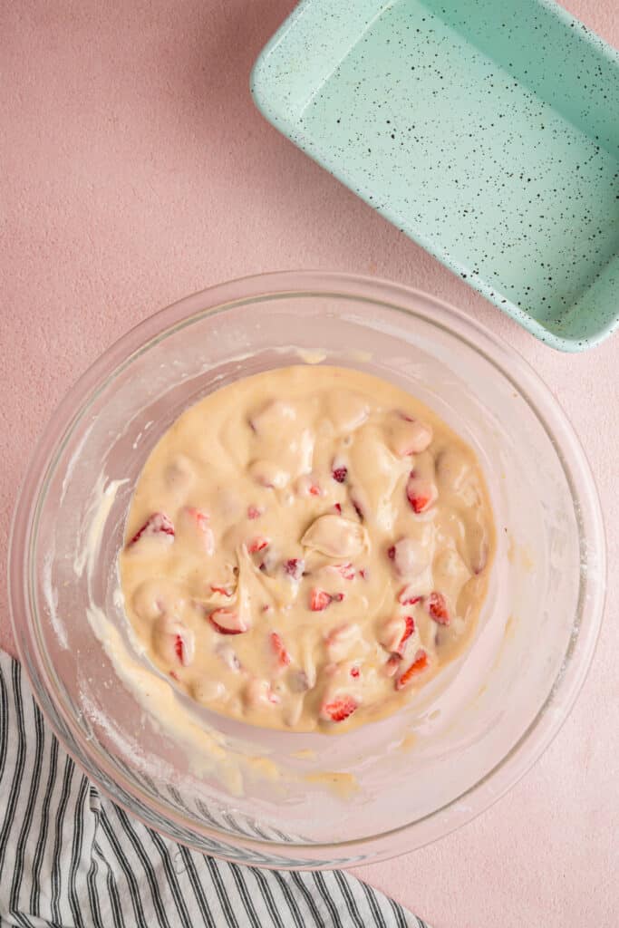 Strawberry bread batter with chopped strawberries in a glass bowl next to an empty loaf pan