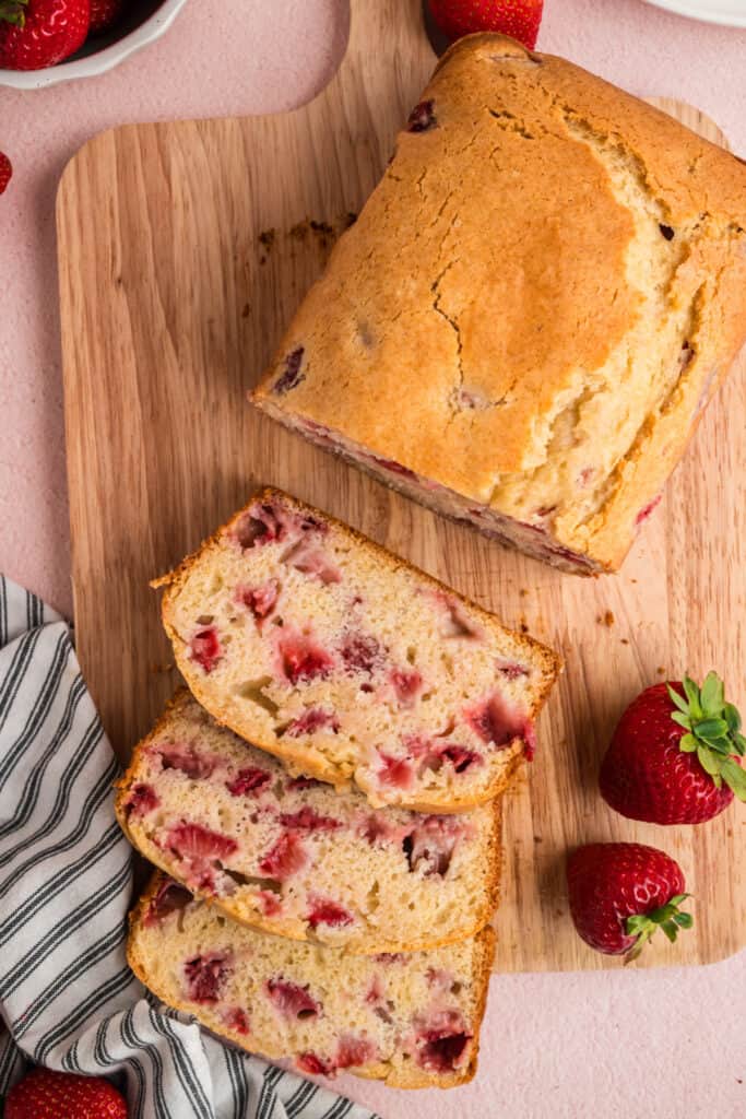 Sliced strawberry bread on a wooden board with fresh strawberries around it
