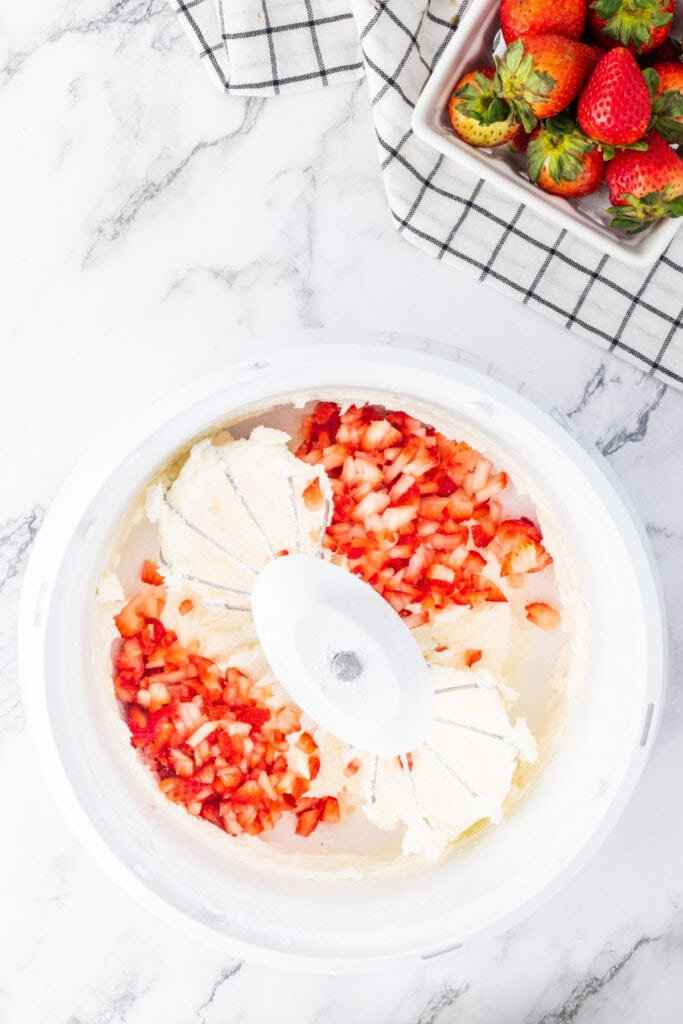 Chopped fresh strawberries added to whipped butter and sugar in a mixing bowl for strawberry frosting.