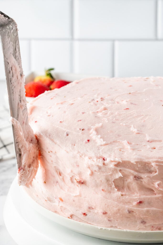 Strawberry cake being frosted with fresh strawberry buttercream using an offset spatula.