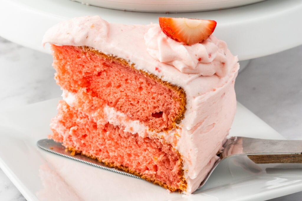 Close-up of a slice of frosted strawberry cake resting on a cake server, ready to be plated.