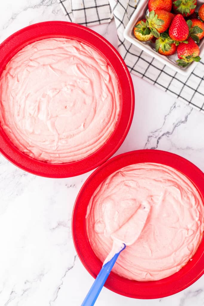 Two red cake pans filled with strawberry cake batter, ready for baking.