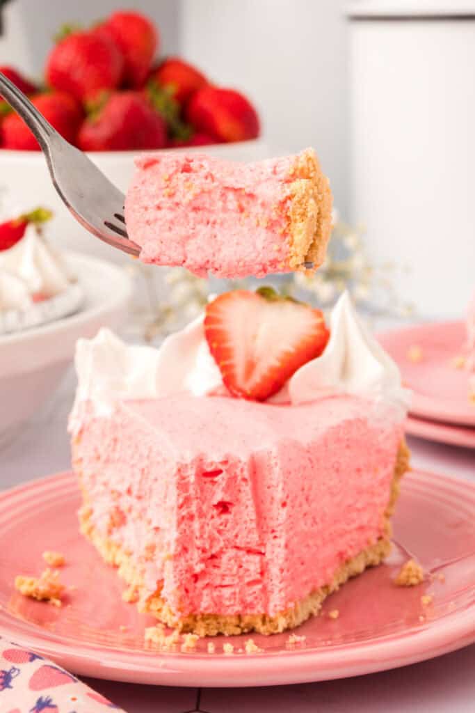 ork holding a bite of strawberry cream pie above a partially eaten slice on a pink plate