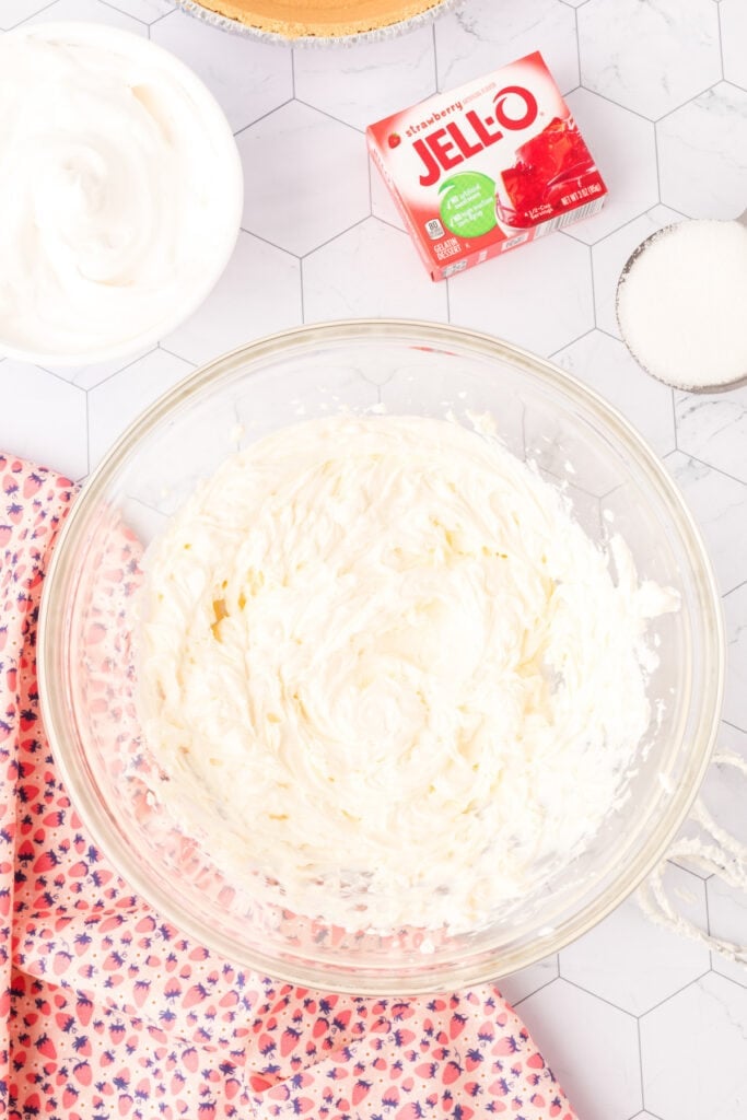 Cream cheese mixture whipped in a clear glass bowl with ingredients nearby