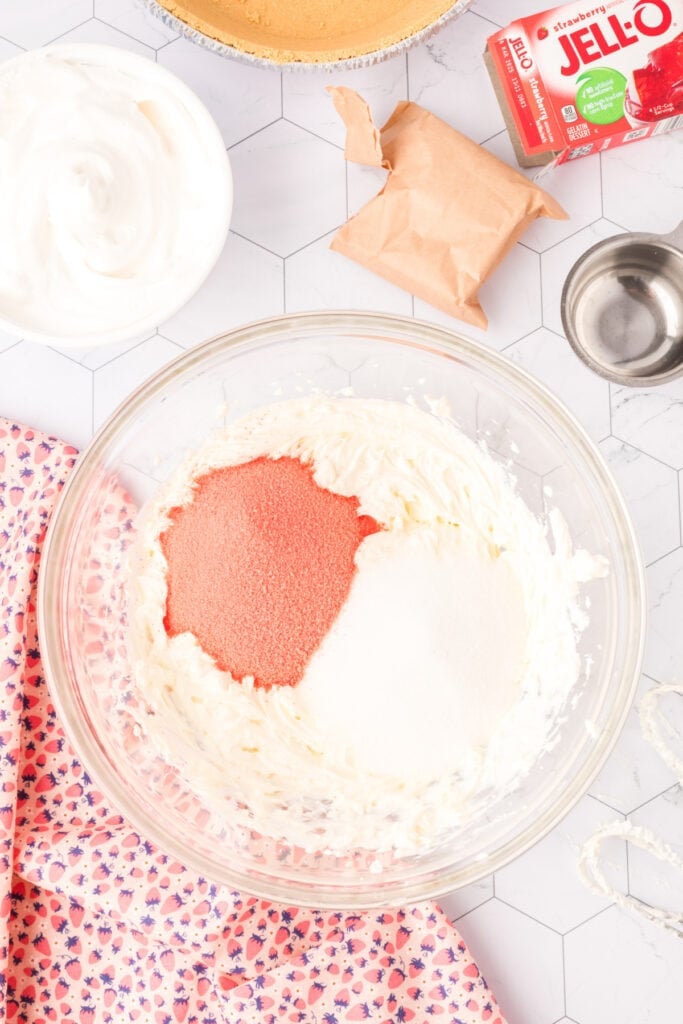 Sugar and dry strawberry Jello poured into the whipped cream cheese mixture in a mixing bowl