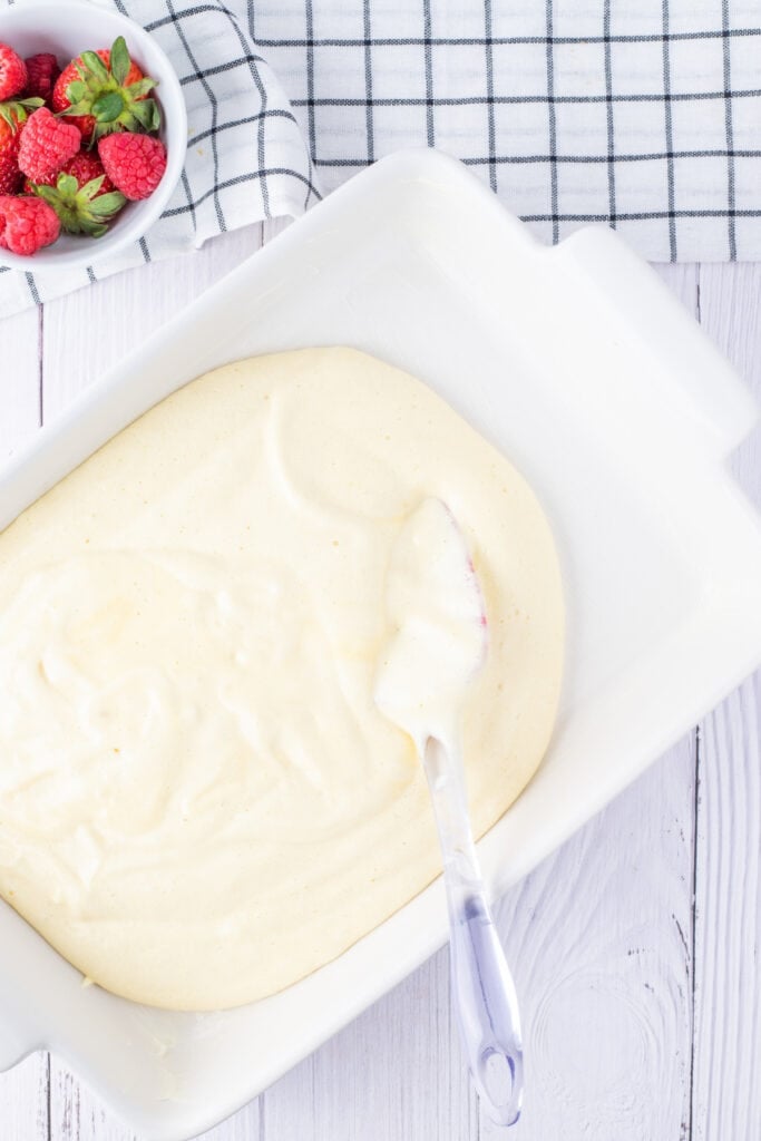 Raw cake batter spread evenly in a white baking dish with a spatula, ready to go into the oven.
