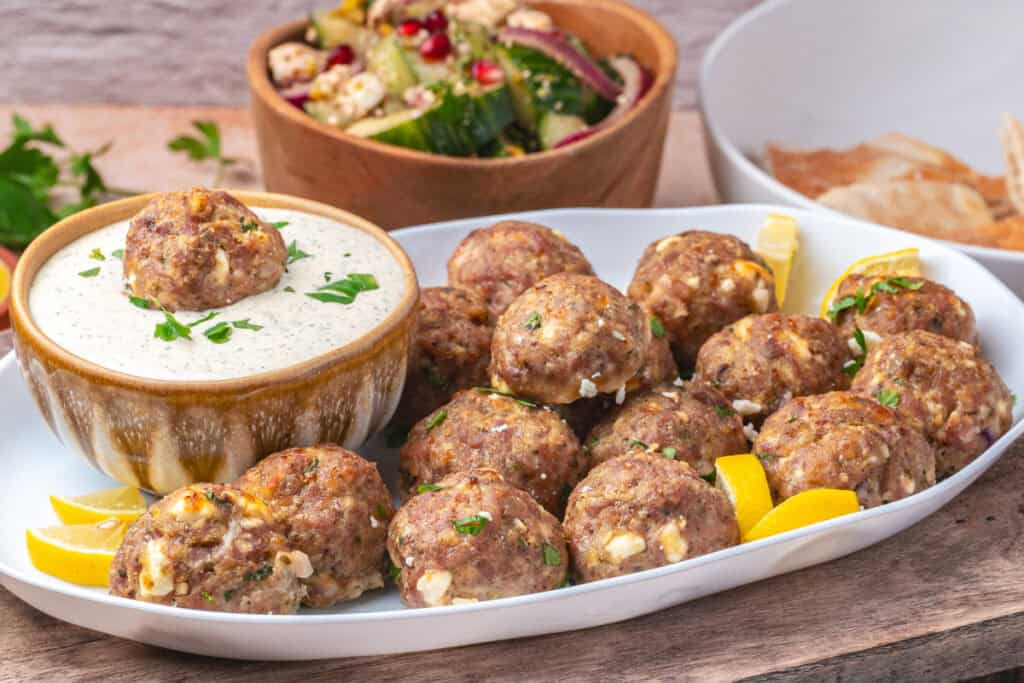 Platter of turkey feta meatballs with dipping sauce and Mediterranean salad in the background