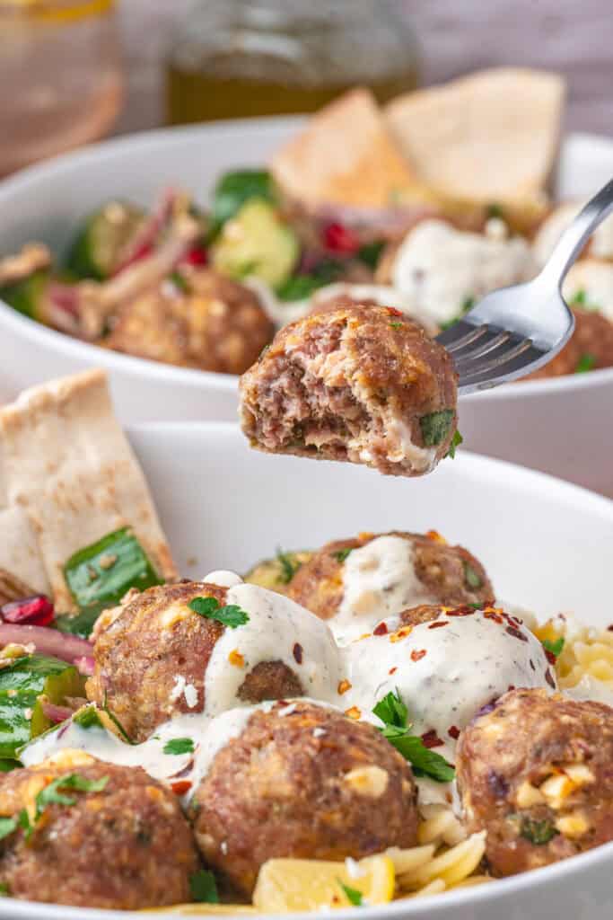 Closeup of a fork holding a turkey feta meatball over a bowl of pasta and salad