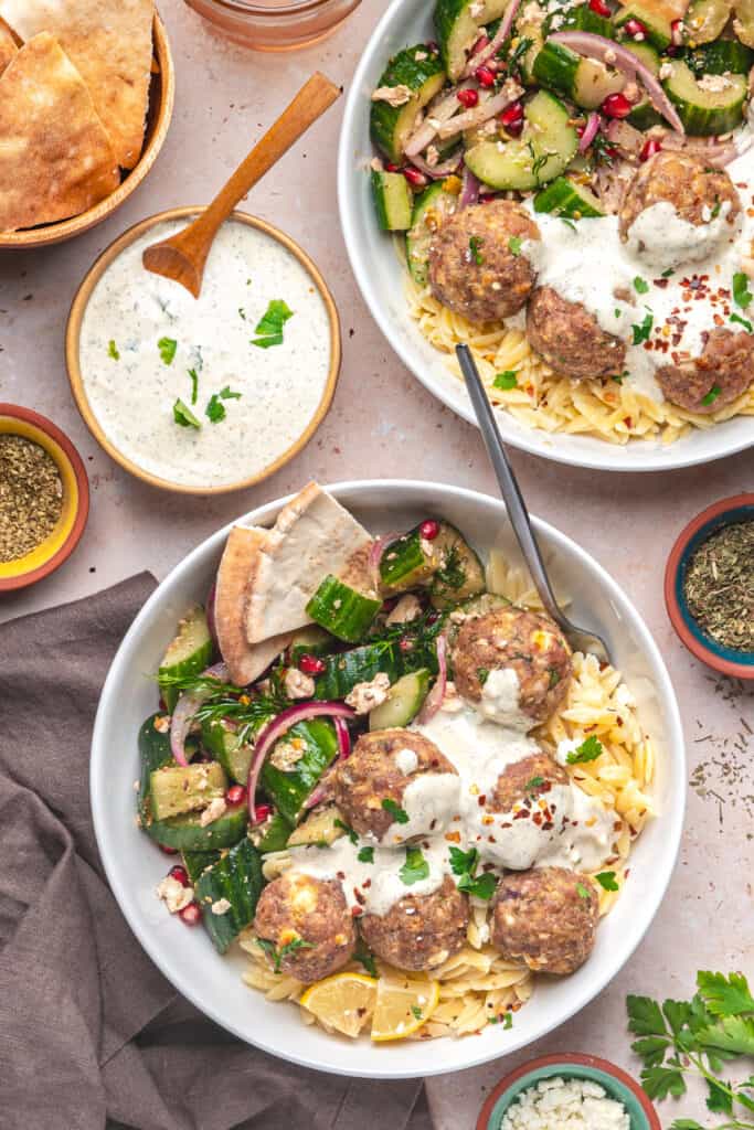 Overhead shot of two bowls filled with turkey feta meatballs, orzo, tzatziki, and cucumber salad