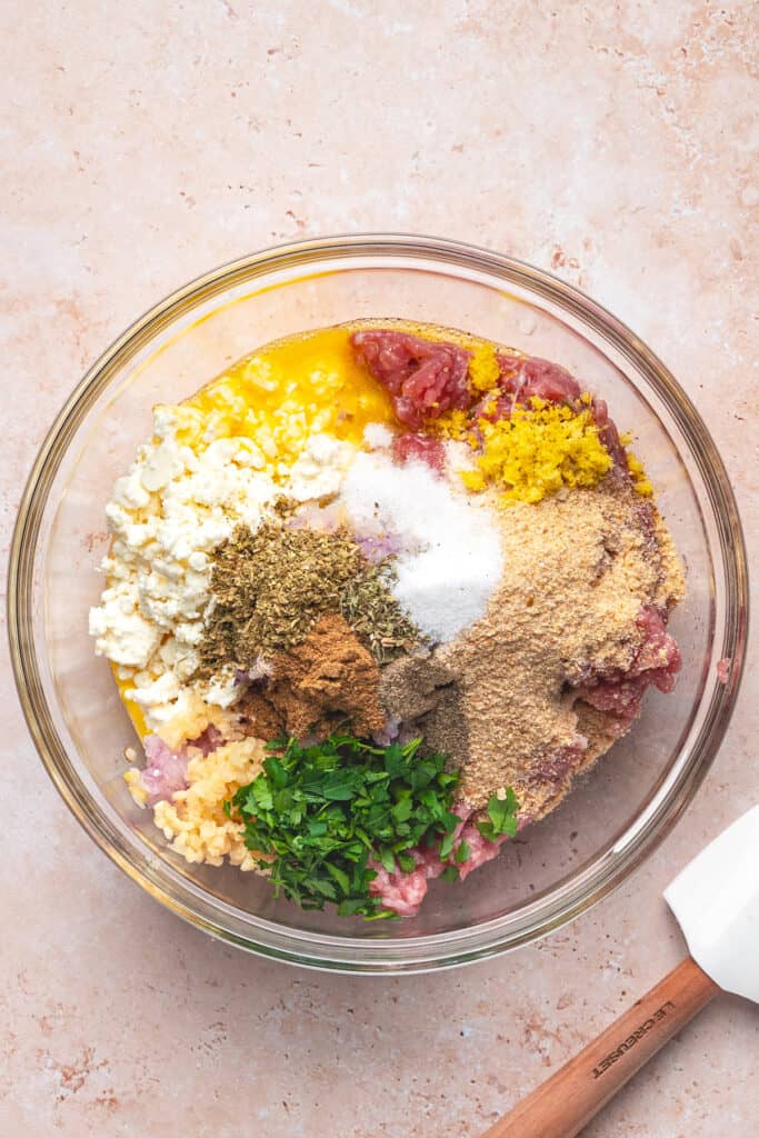 Bowl with ground turkey, feta, herbs, lemon zest, and other ingredients before mixing