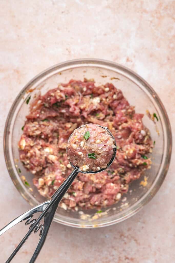 Cookie scoop holding a portion of turkey feta meatball mixture over the bowl