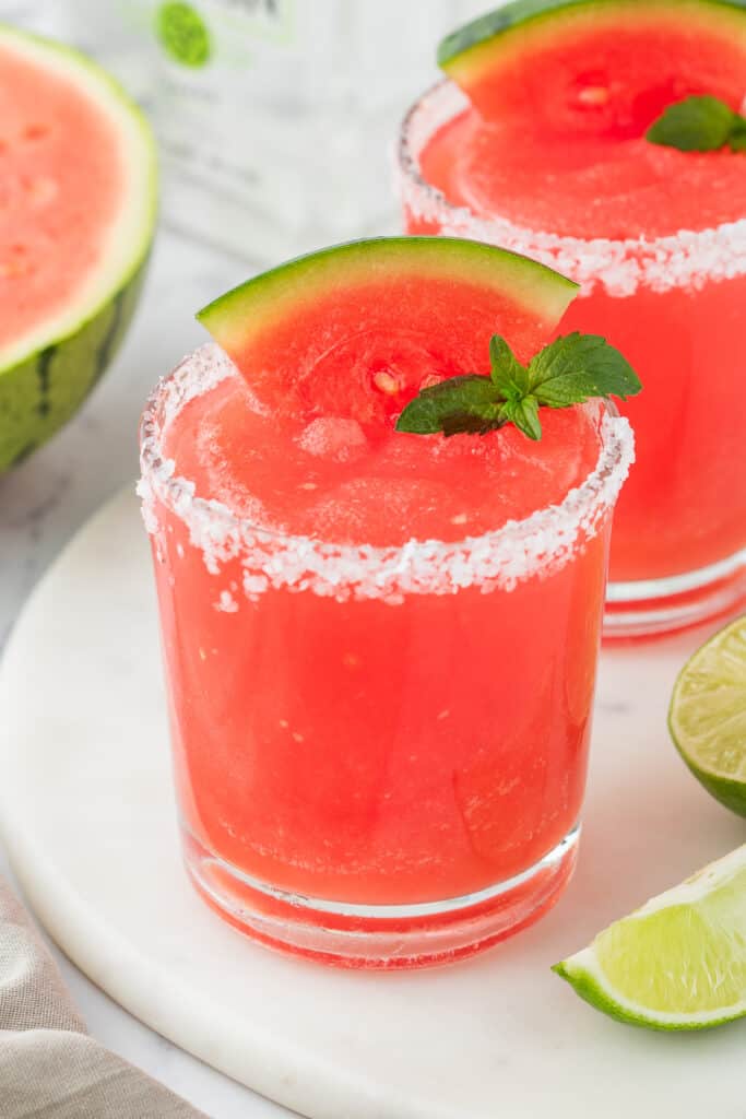 Close-up of a salted-rim glass filled with frozen watermelon margarita, garnished with a watermelon wedge and mint