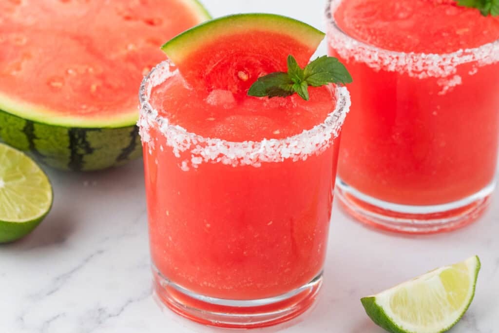 Watermelon margaritas garnished with fresh mint and watermelon, with lime and watermelon in background