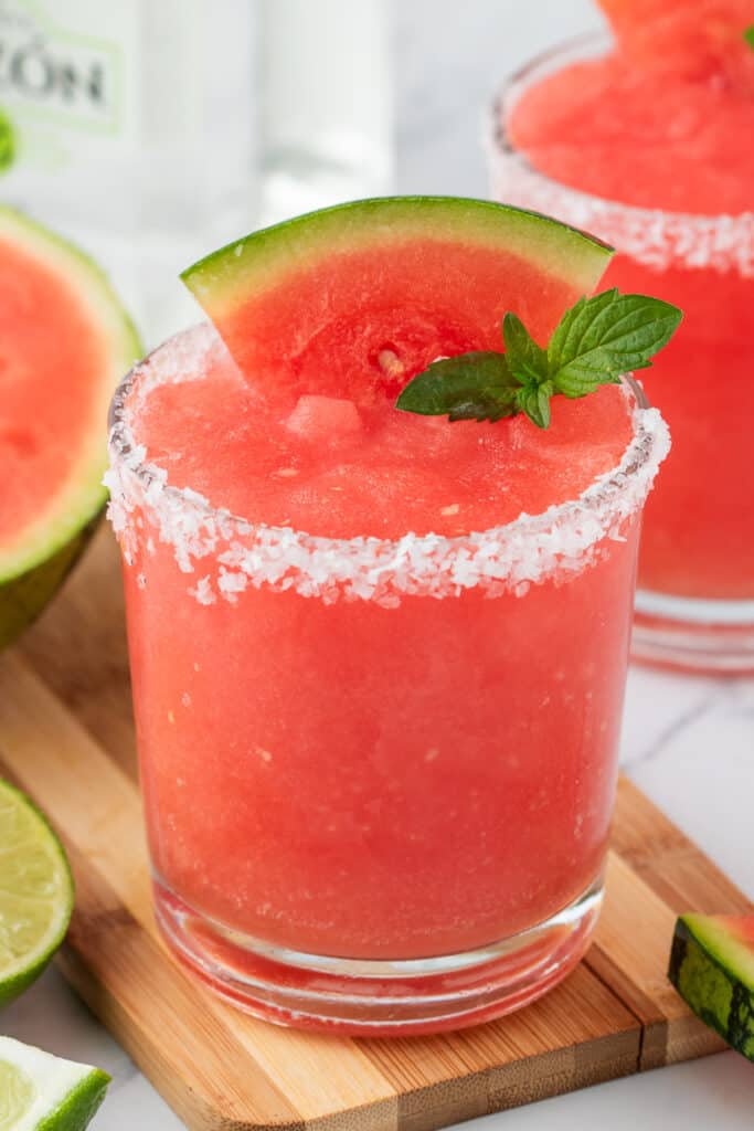 Watermelon margarita served on a wooden board, garnished with mint and a watermelon wedge